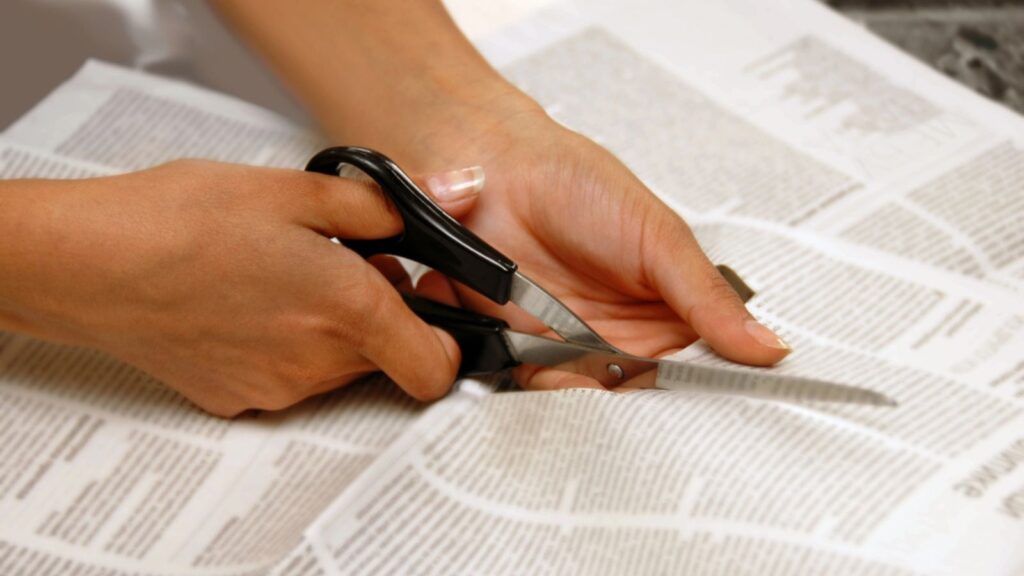 Hands with scissors cutting out an article from newspapers