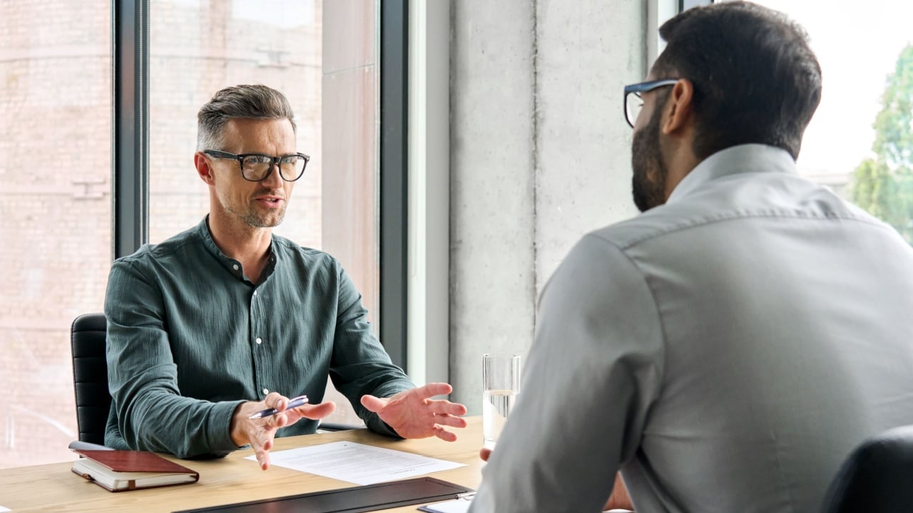 Two diverse business executive partners negotiating at board meeting, manager adviser consulting client discussing financial partnership contract sitting at table in office. Job interview concept.