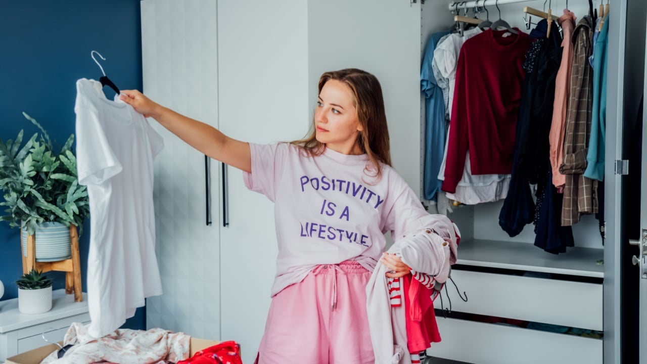 Woman selecting clothes from her wardrobe for donating to a Charity shop. Decluttering, Sorting clothes and Cleaning Up. Reuse, second-hand concept. Conscious consumer, sustainable lifestyle.