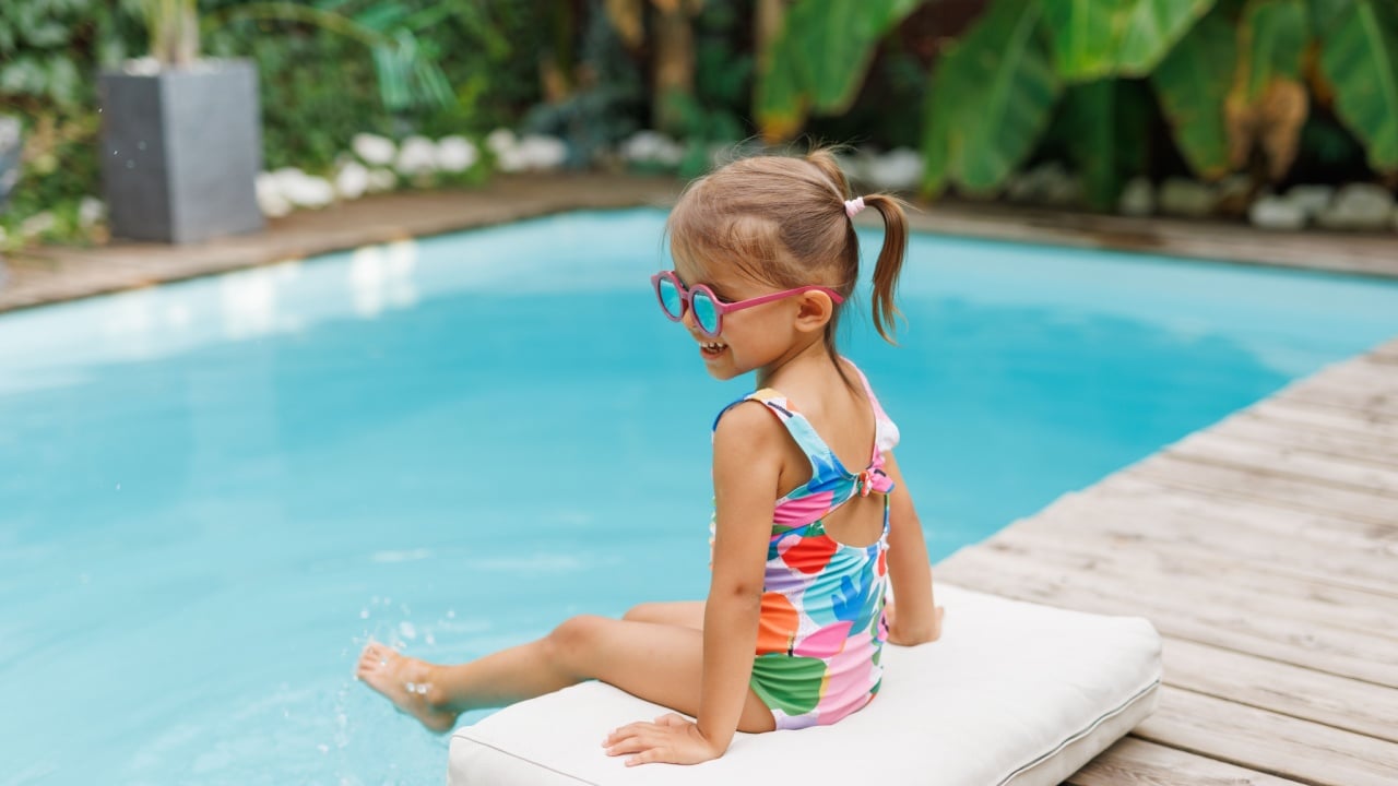 Funny cute girl on summer vacation. The child has fun near the pool. Cute baby girl in a colorful swimsuit and sunglasses is resting.