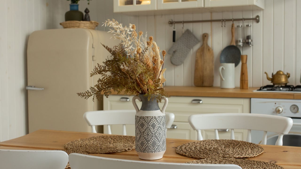 Cozy kitchen in light home interior, photo of country house in natural style, kitchen table, fridge, vase with dried flowers and kitchenware