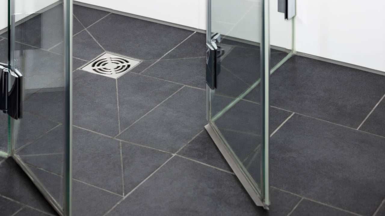 Floor Drain Metal Hole for Draining Water in Modern Shower Cabin in Bathroom with Ceramic Tiles and Glass Shower Door. Close-up.